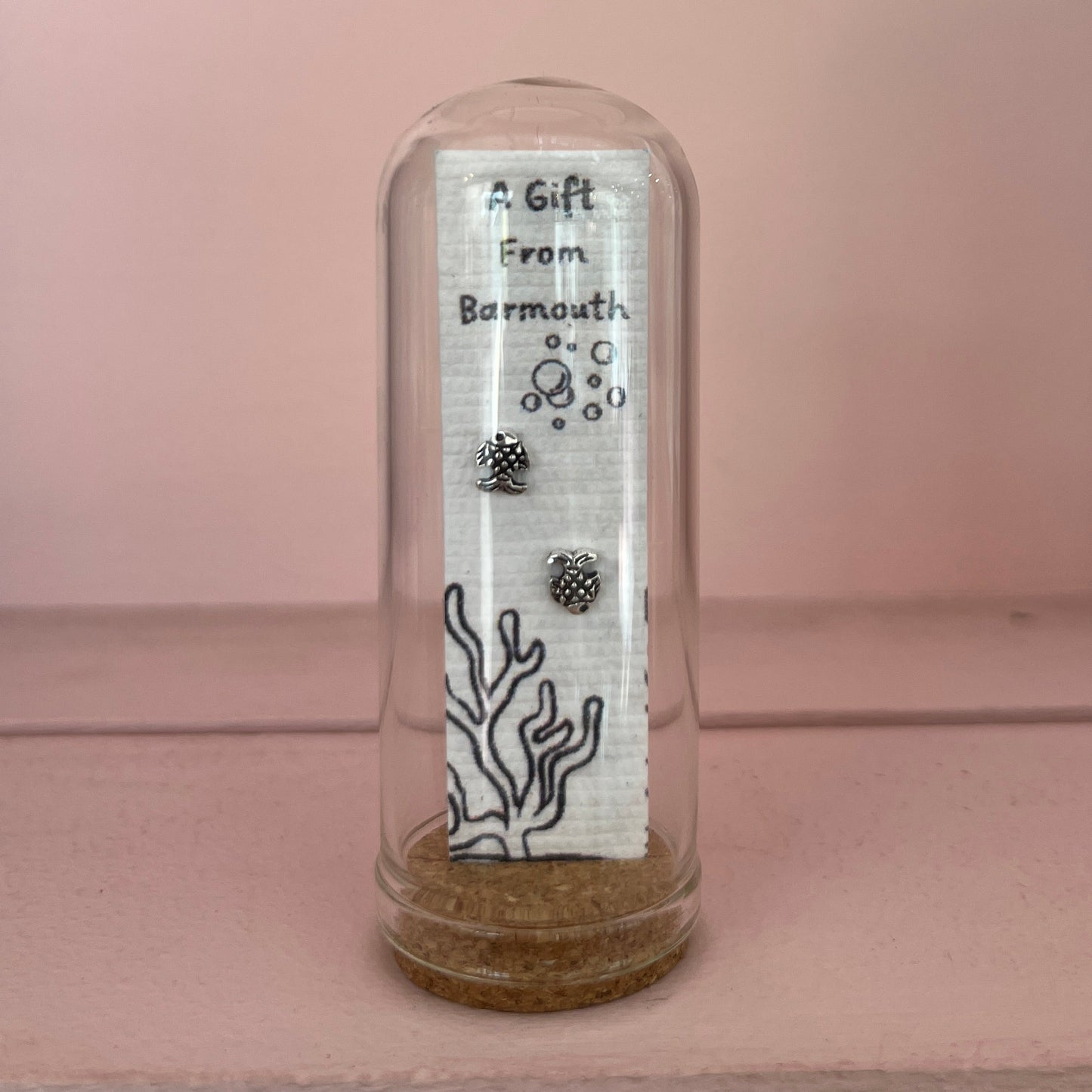 Two small silver charms inside a clear glass dome with a label on a pink background