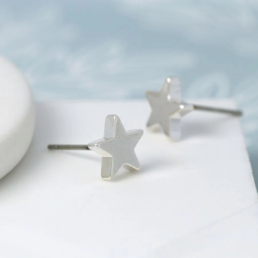 Silver star-shaped earrings on a white surface with a light blue background
