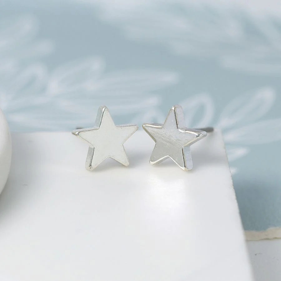 Silver star earrings on a white surface with a light blue background