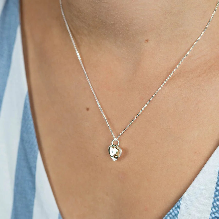 Silver necklace with a heart pendant on a person wearing a blue and white striped shirt.