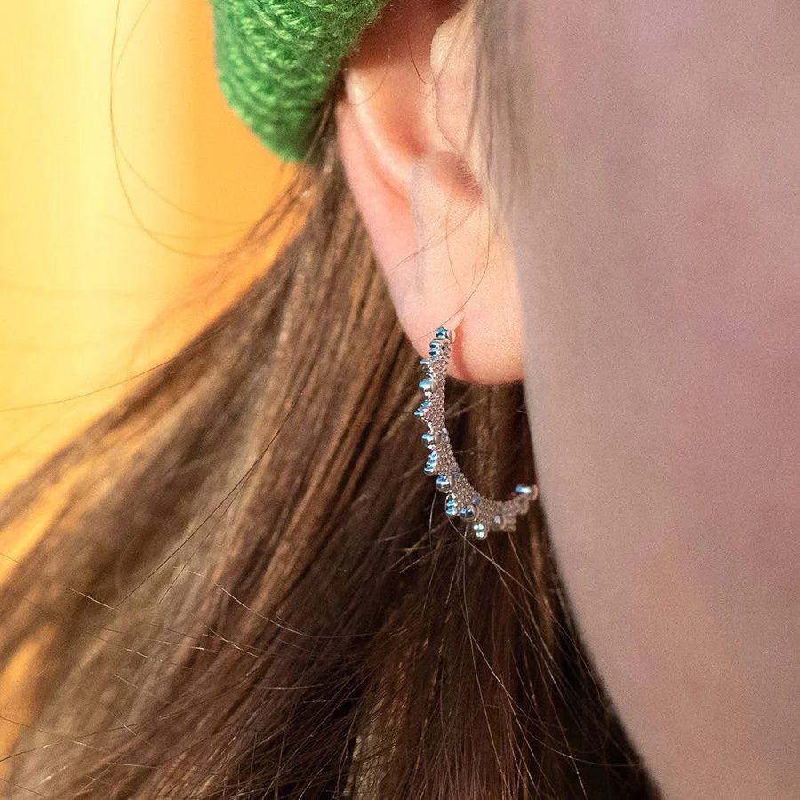 Close-up of an ear wearing a decorative hoop earring with a blurred background