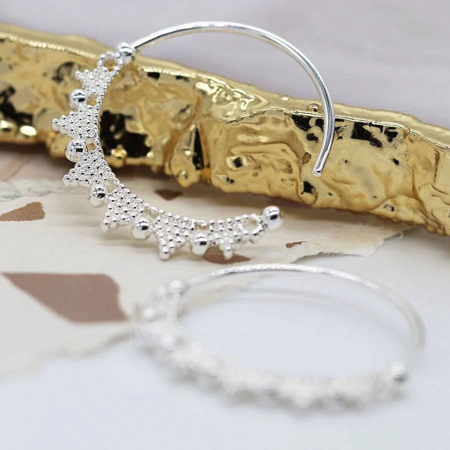 Silver hoop earrings with intricate designs on a textured gold surface.