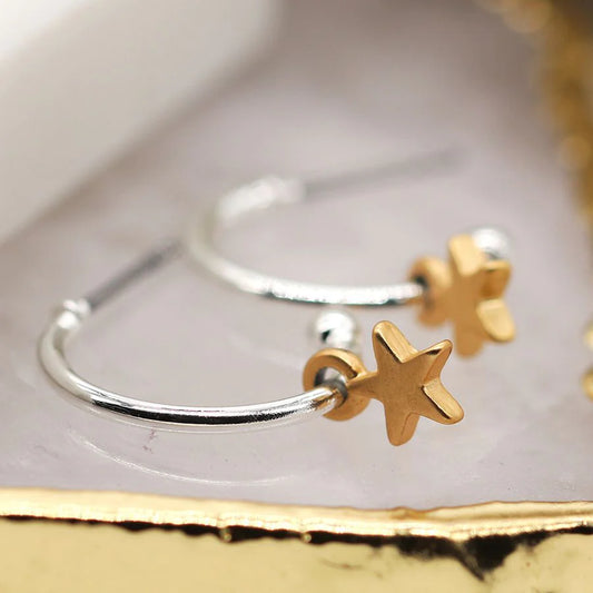 Silver plated earrings with gold star charms on a gold surface