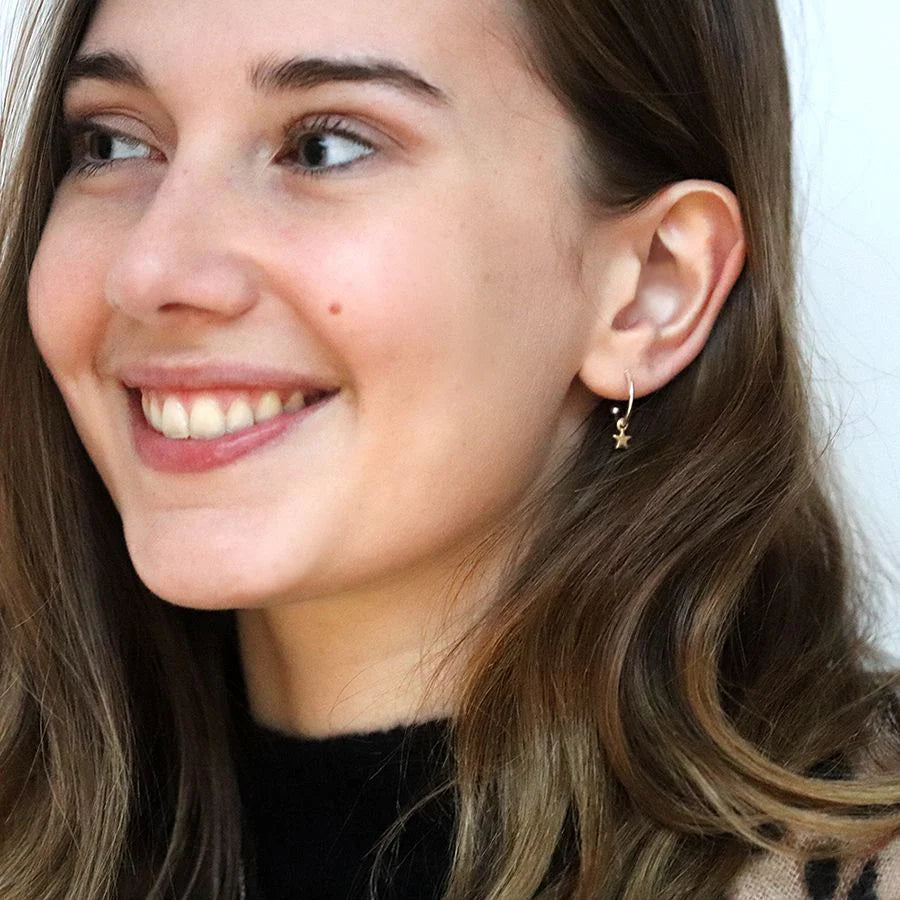 Close-up of a woman wearing a gold hoop earring with a star design.