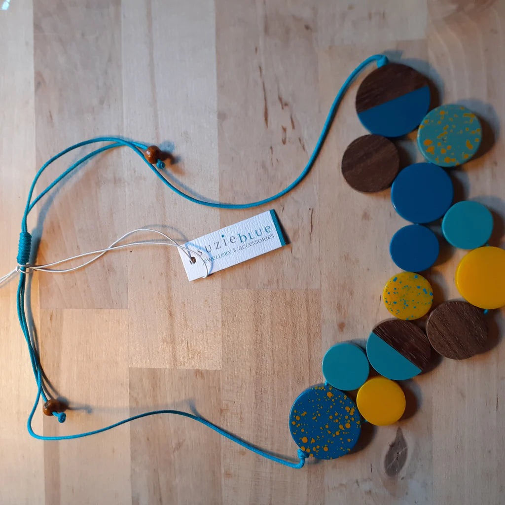 Necklace with colorful circular pendants on a wooden surface, featuring a 'Zuzieblue' tag.