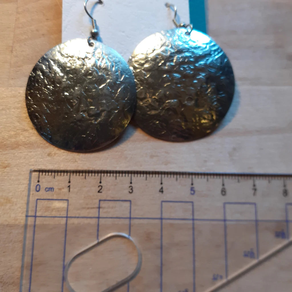 Pair of textured silver earrings on a wooden surface with a ruler for scale.
