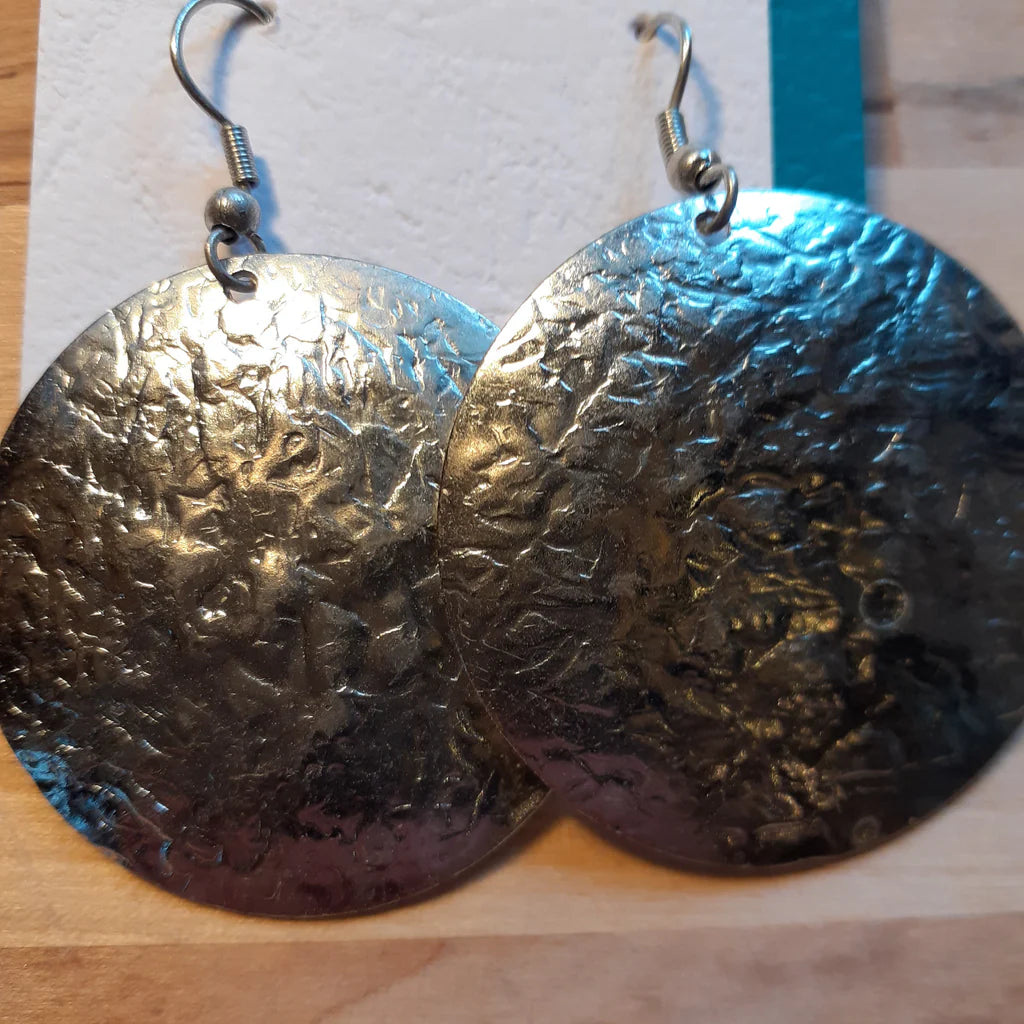Pair of textured silver coloured earrings on a wooden surface