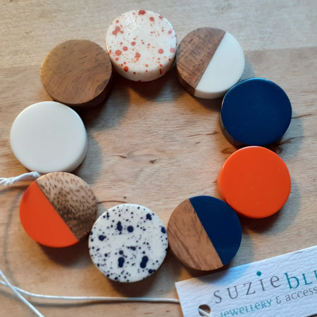 Colorful round wooden earrings on a wooden surface with a 'Suzie Blue' tag.