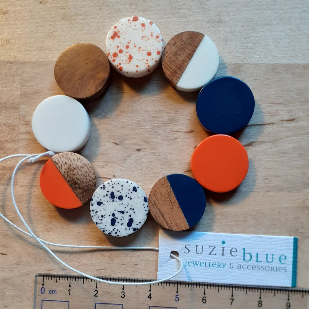 Colorful circular jewelry pieces on a wooden surface with a 'Suzie Blue' tag.