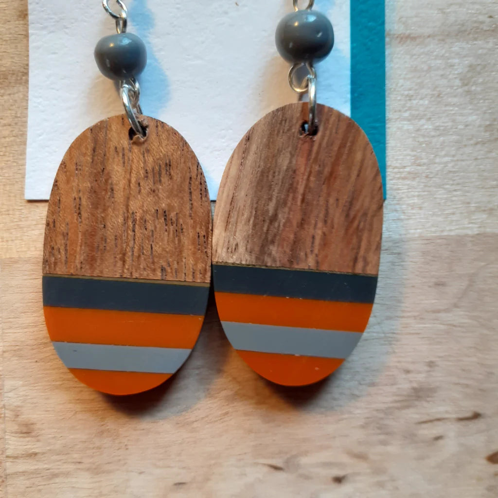 Wooden earrings with orange and gray stripes on a wooden surface