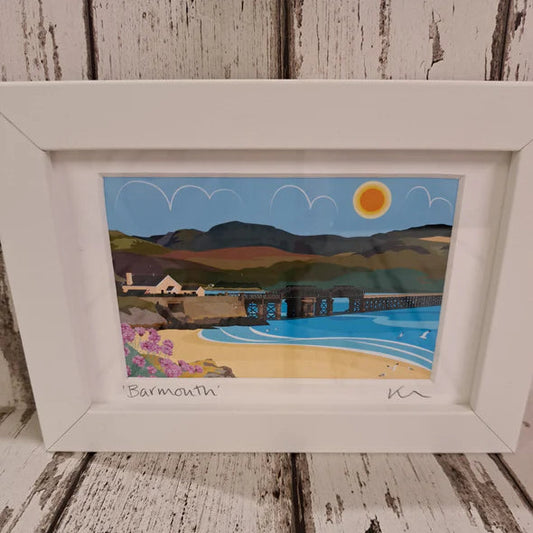 Framed artwork of a coastal scene with mountains and a beach.