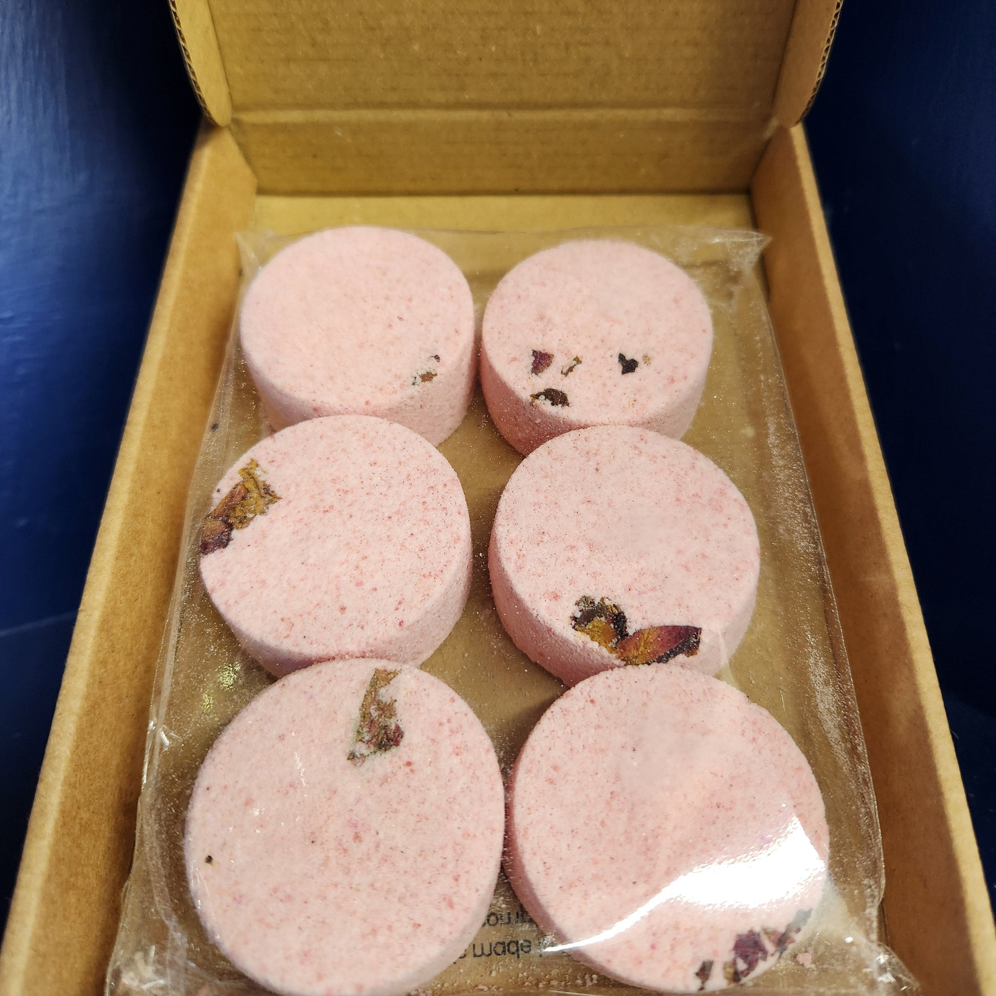 Pink round shower steamers in a cardboard box with clear plastic wrap.