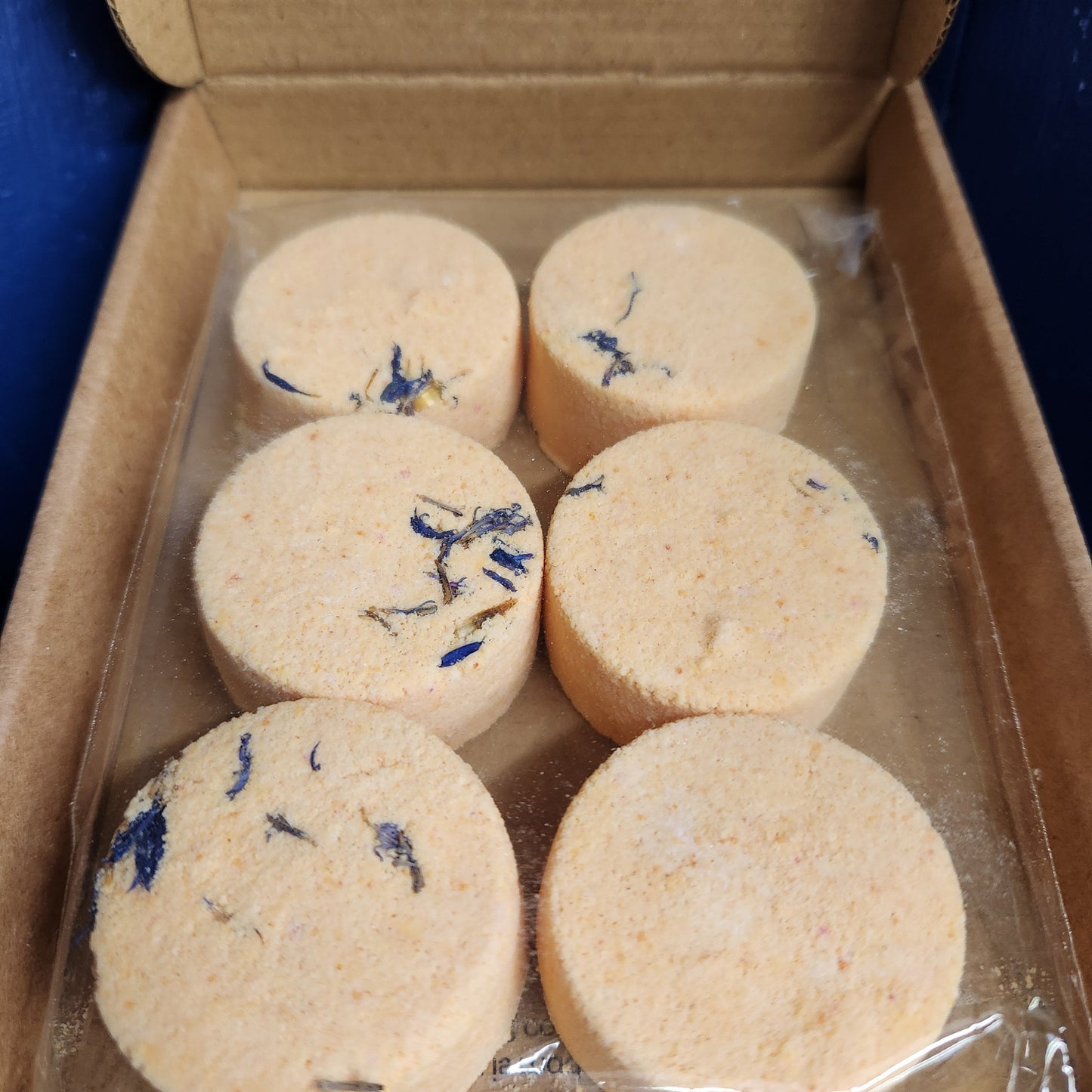 Six round cookies with blue specks in a cardboard box.