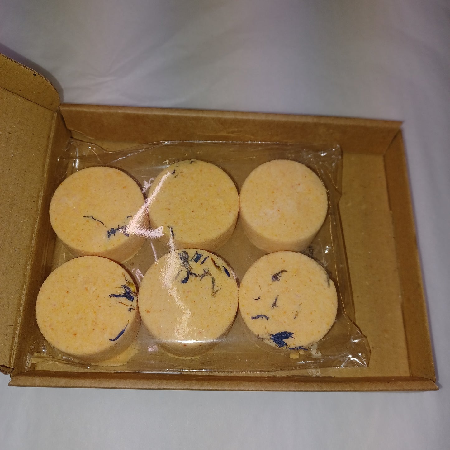 Five yellow circular items with blue patterns in a clear plastic wrap inside a cardboard box.