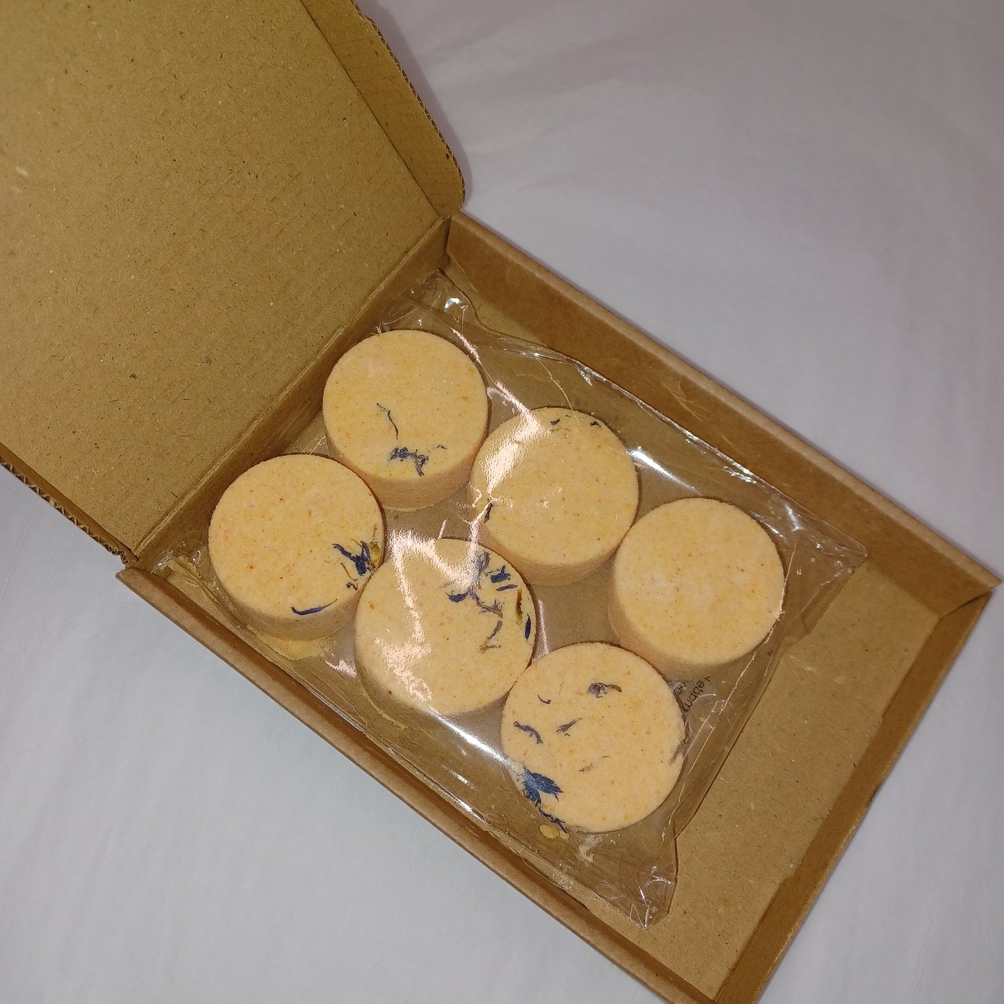 Six round yellow items with blue designs in a clear plastic bag inside an open cardboard box.