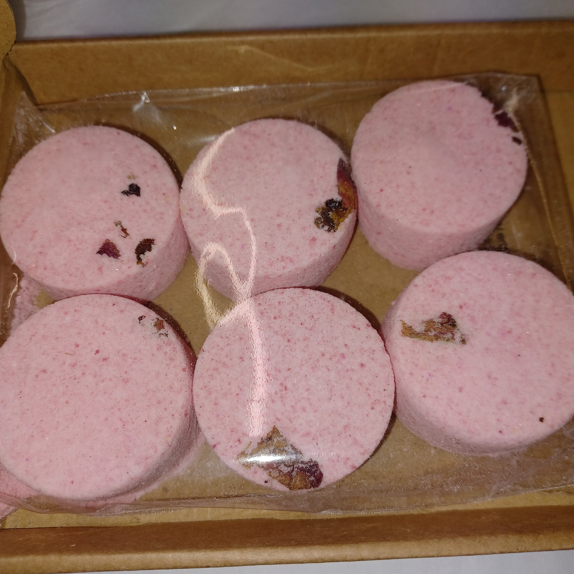 Pink shower steamers with visible ingredients in a clear plastic bag on a cardboard base.