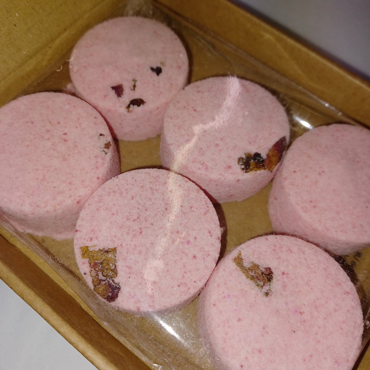 Pink shower steamers with visible specks in a clear plastic bag on a wooden surface.