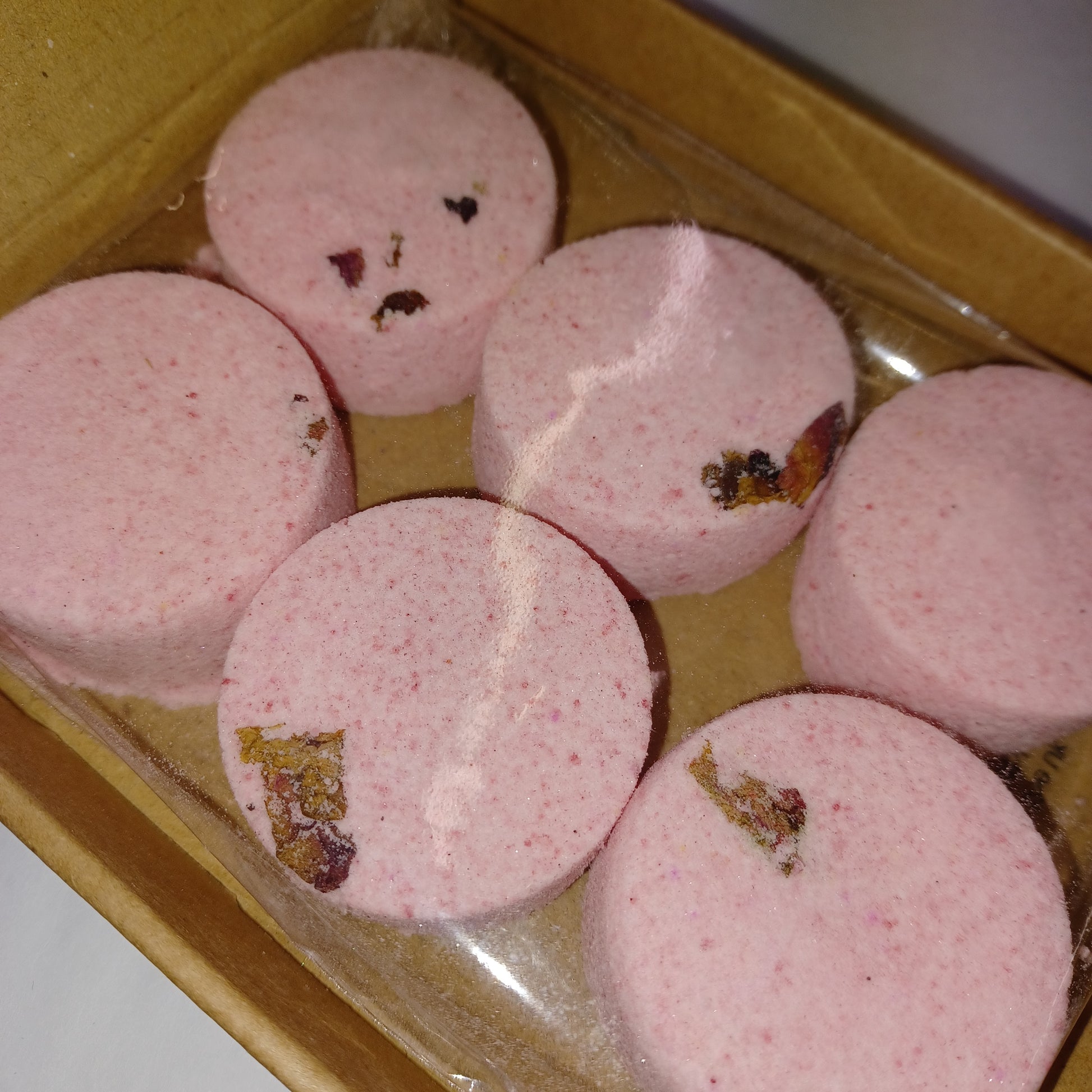 Pink shower steamers with visible specks in a clear plastic bag on a wooden surface.