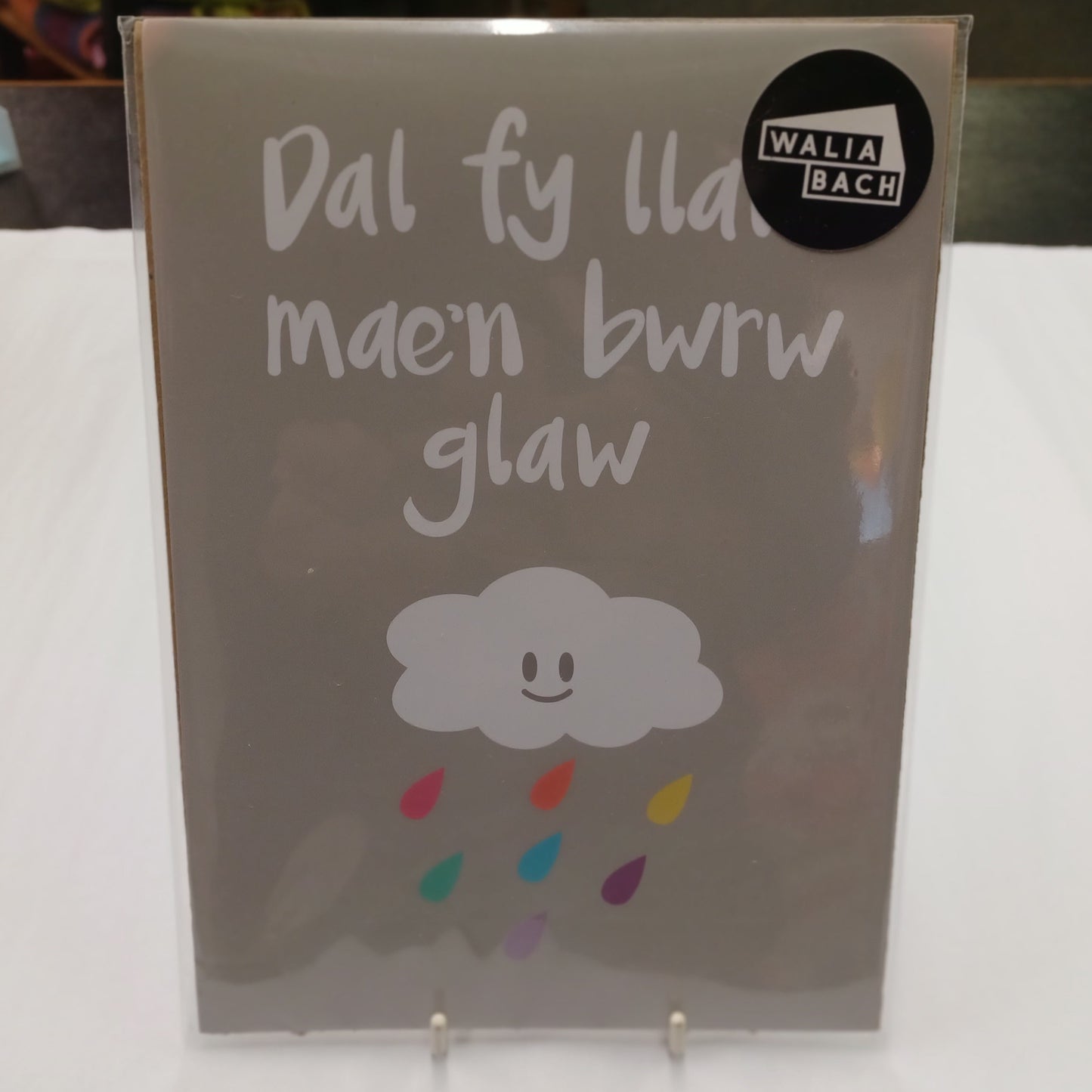 Notebook with Welsh text and a cloud design on a white surface