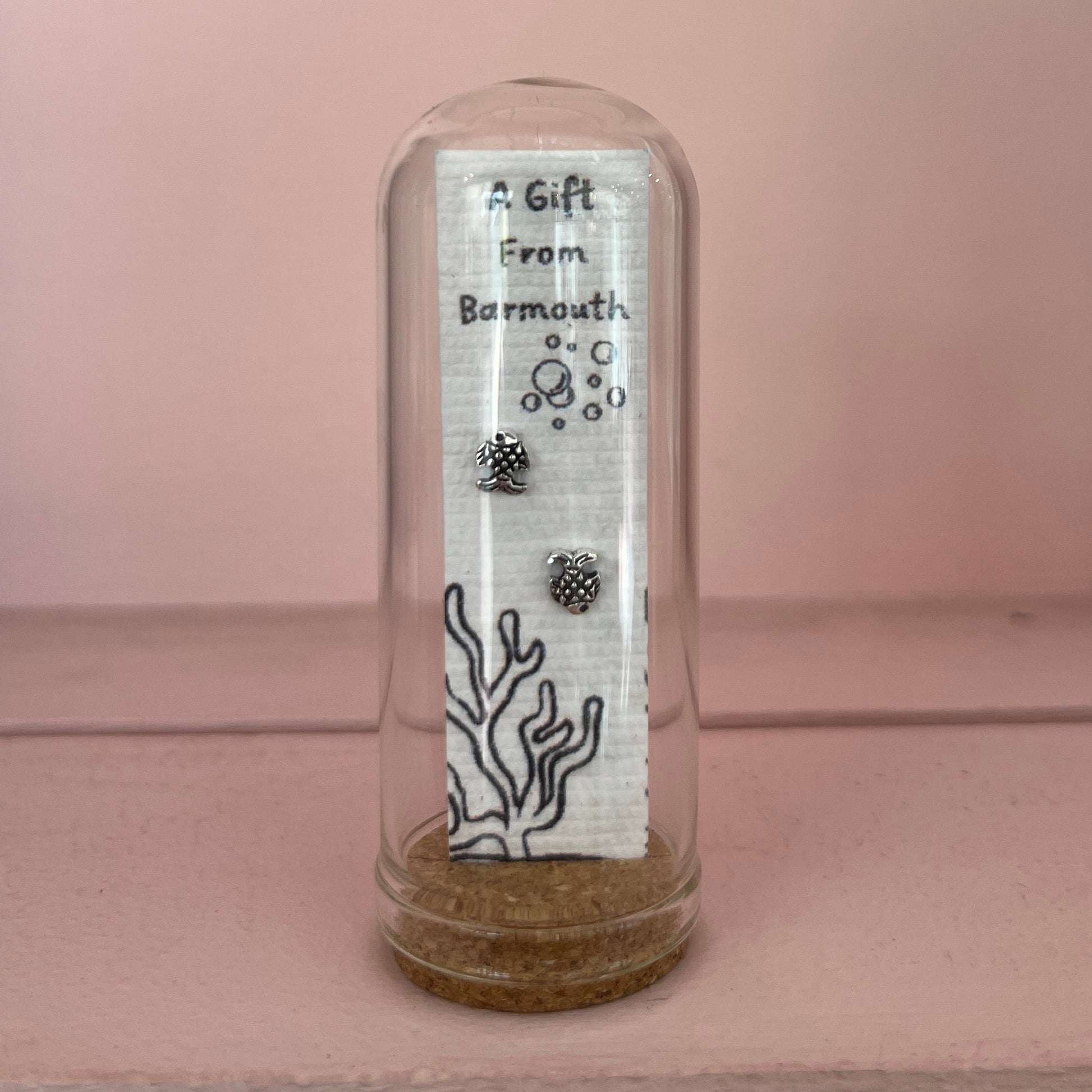 Two small silver charms inside a clear glass dome with a label on a pink background