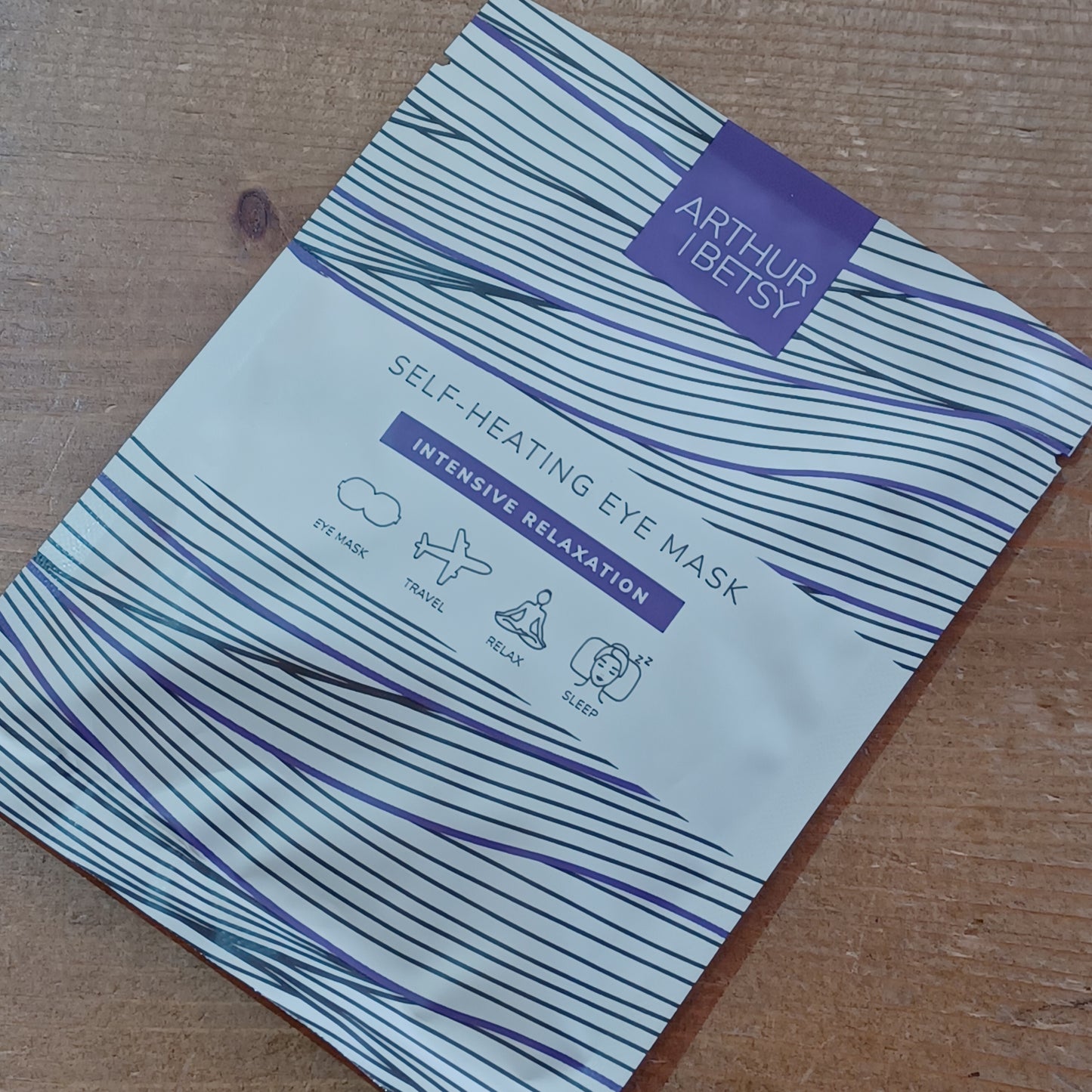 Self-heating eye mask packaging with blue and white design on a wooden surface