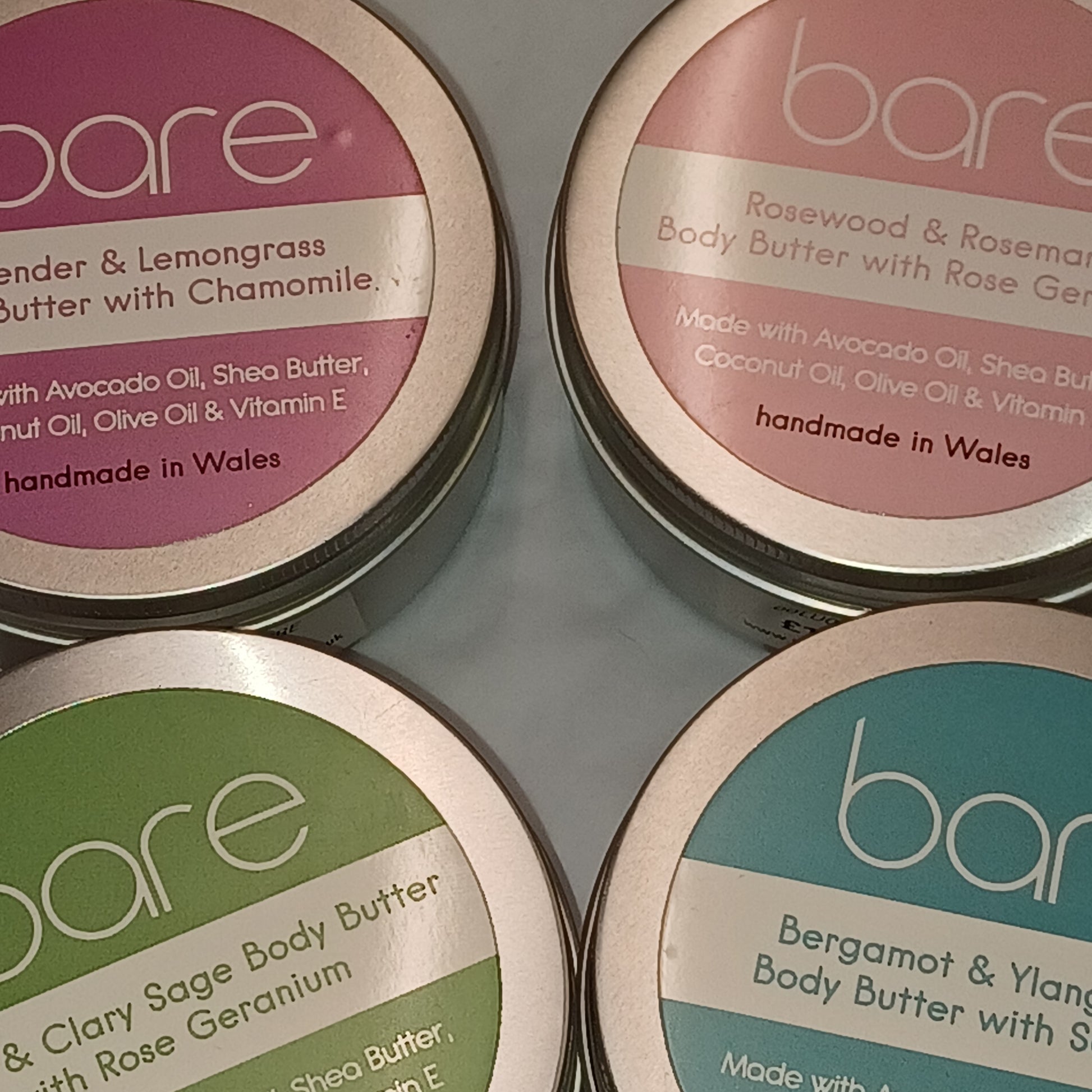 Four tins of bare body butter with different scents on a gray background