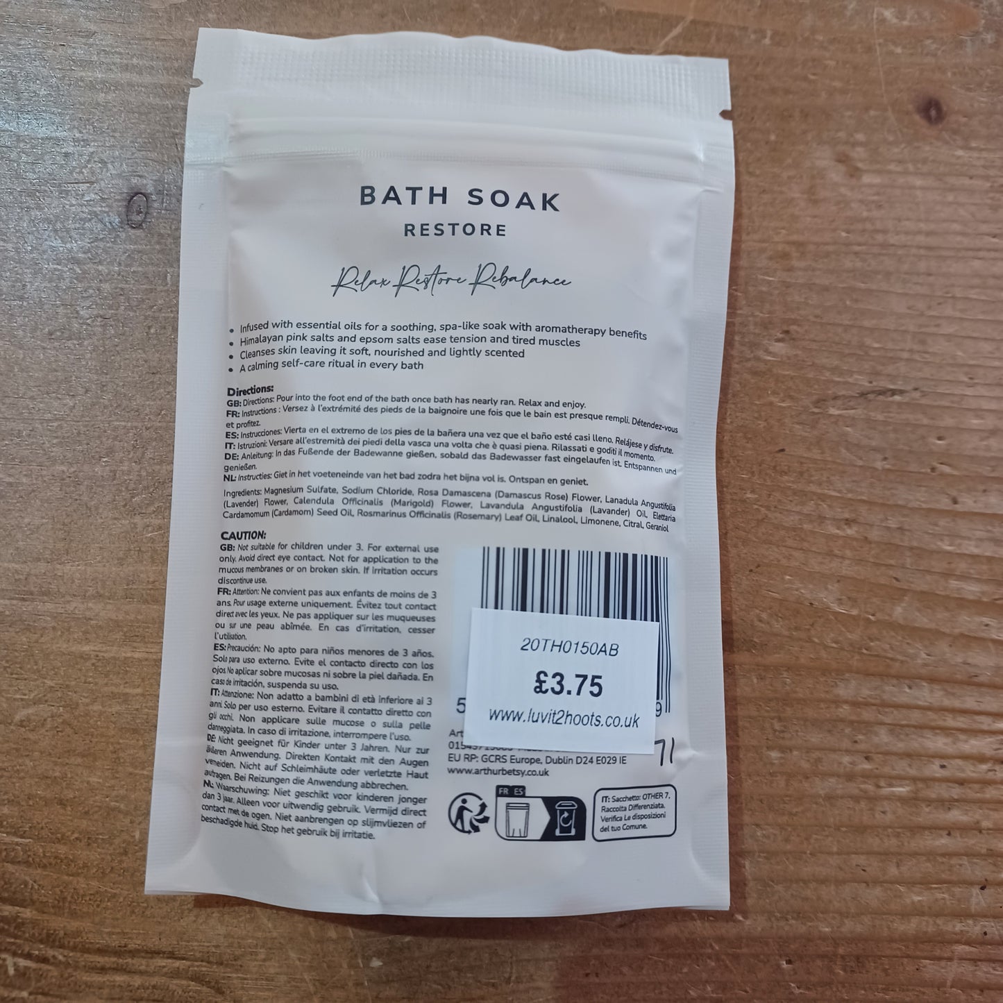 White bath soak packet with text and a barcode on a wooden surface