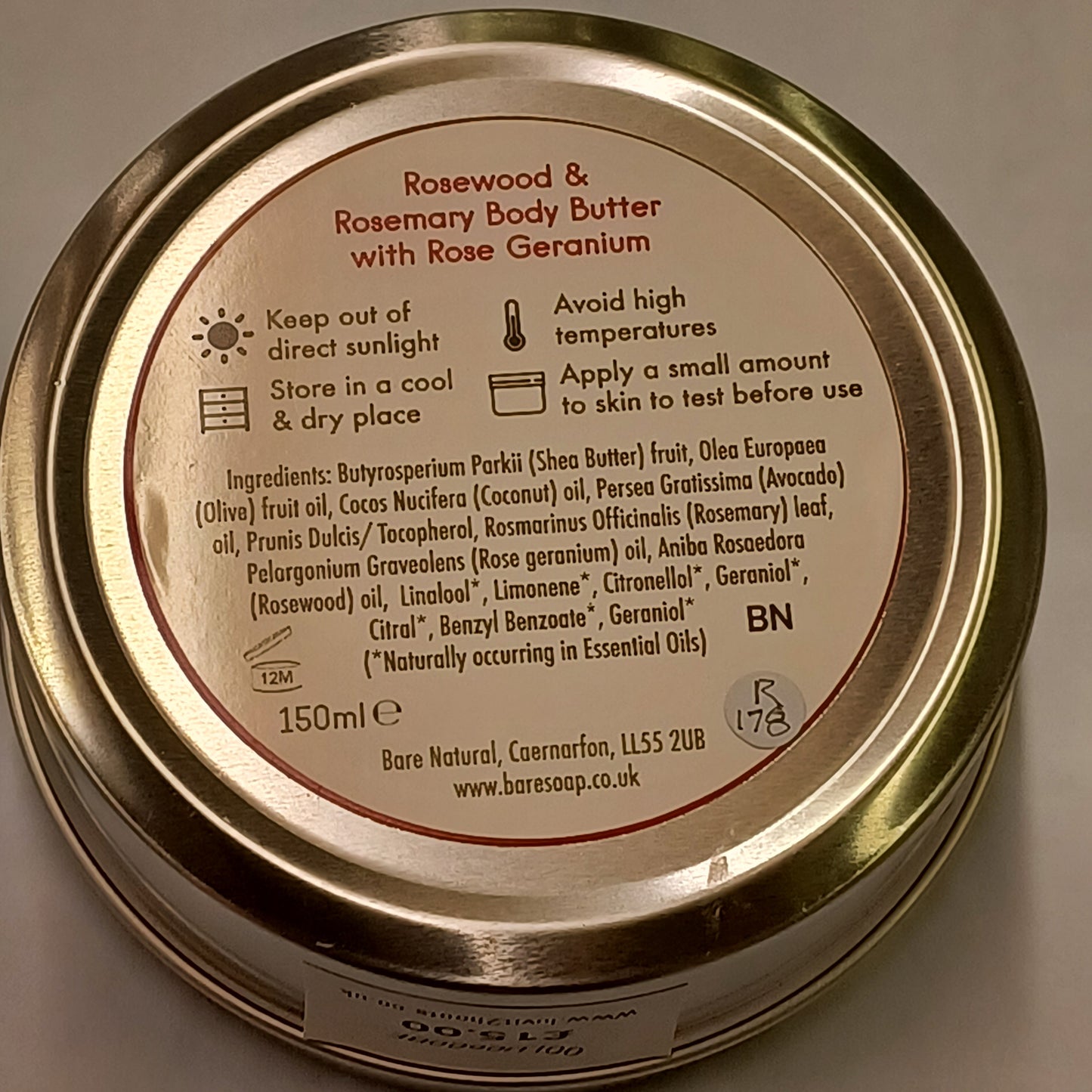 Close-up of a gold jar lid with text and branding on a neutral background